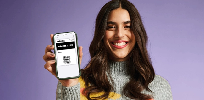Ein Foto zeigt eine Frau, die ein iPhone mit der WÖHRL Loyalty Card in Apple Wallet hält.