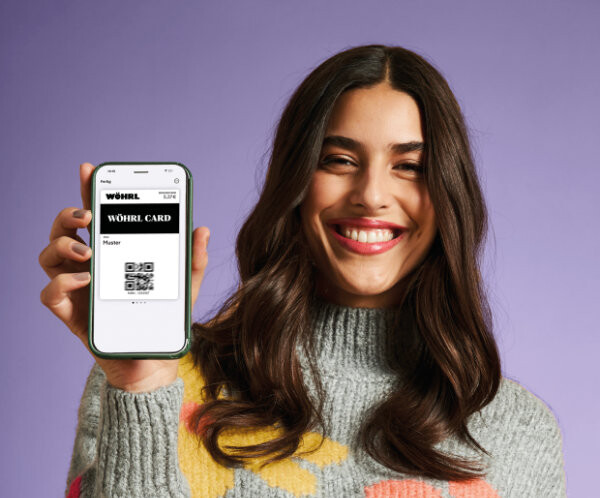 Ein weiteres Bild zeigt eine Frau, die die digitale WÖHRL Card in Apple Wallet auf einem iPhone präsentiert.