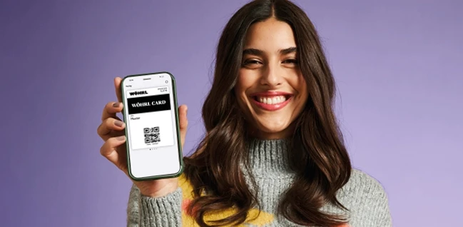 A woman holding an iPhone showing the WÖHRL Loyalty card in Apple Wallet